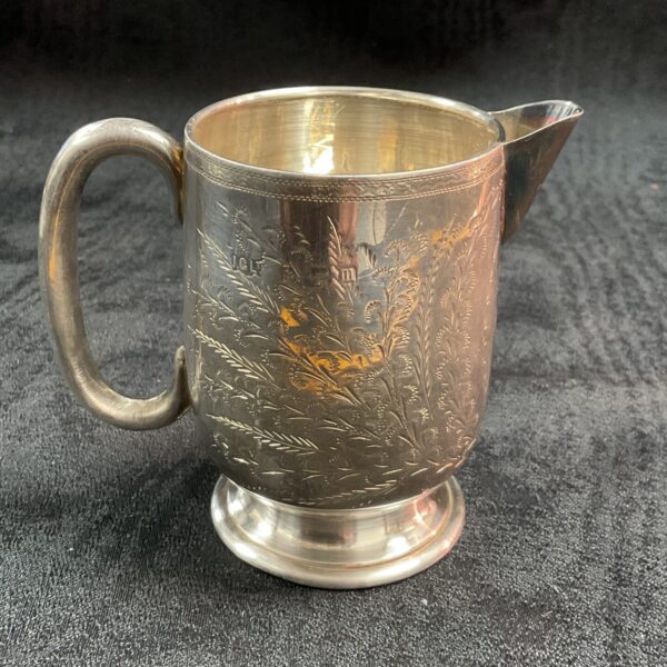 Antique sterling silver cream jug with embossed floral design.