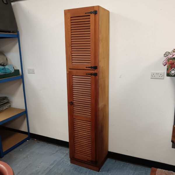 Front view of a tall pine cabinet with louvered doors.