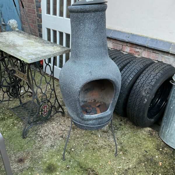 Terracotta garden chimenea standing on a patio with other garden items.