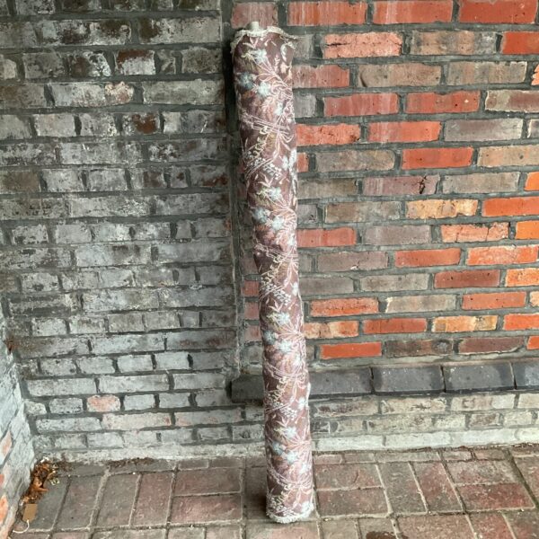 Vintage floral fabric roll displayed against brick wall.