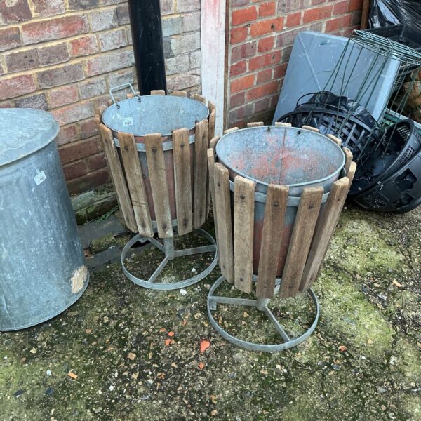 Two vintage galvanised waste bins in a garden setting.