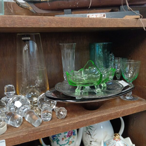 Vintage green glass dish on a wooden shelf with other glassware.