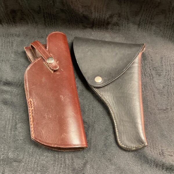 Two vintage leather pistol holsters displayed against a dark background.