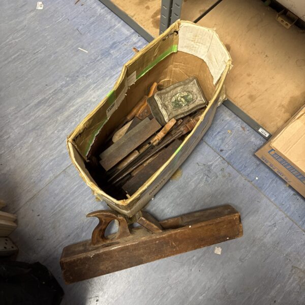 Vintage woodworking tools in a cardboard box, antique planes and chisels.