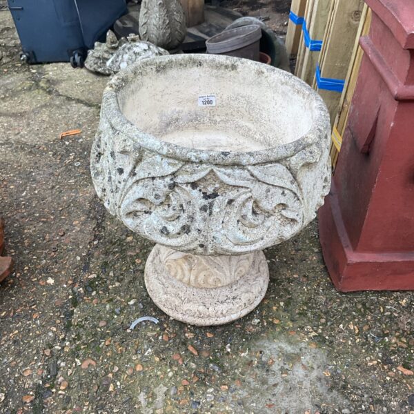 Weathered stone garden urn on a paved surface.