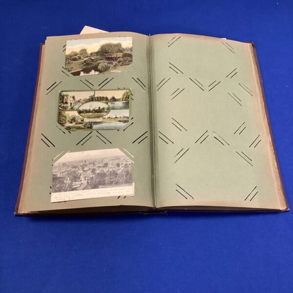 Open antique postcard album displaying vintage postcards and patterned pages.