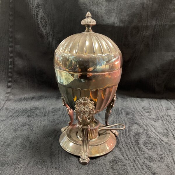 Ornate antique silver plate egg coddler on a dark background.