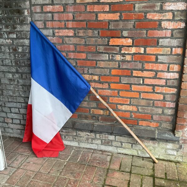 Large vintage French flag on bamboo pole, vibrant tricolore.