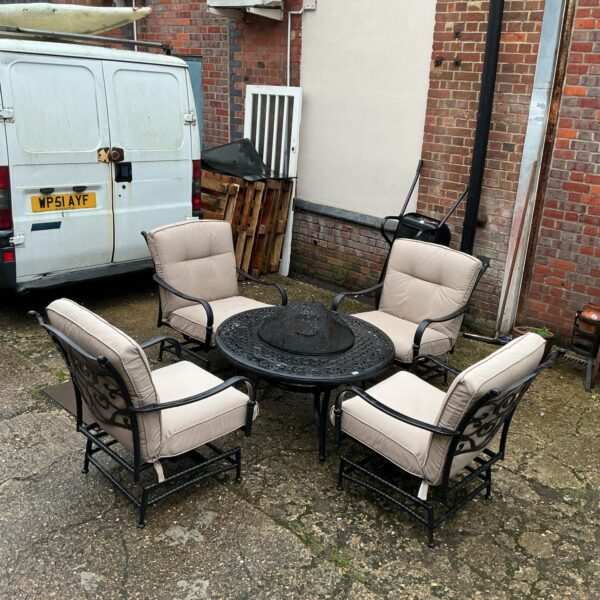 Garden fire pit set with four metal chairs and cushions.