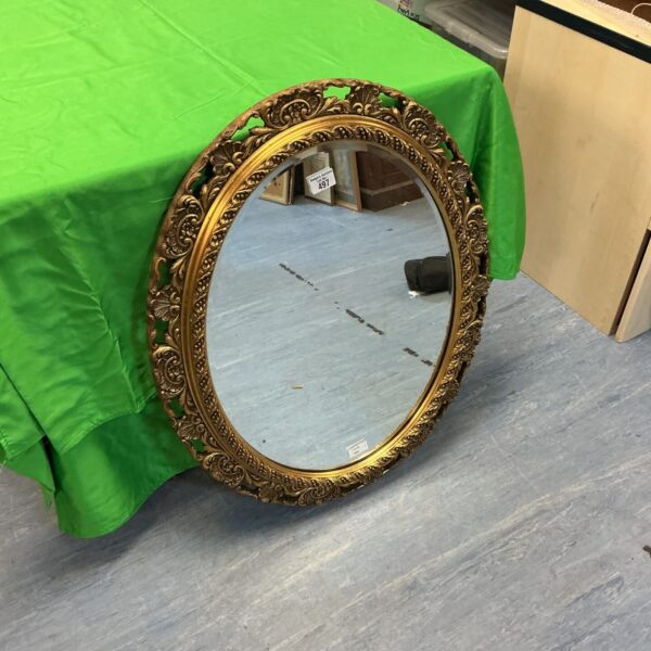 Ornate gilt framed oval bevel edge mirror for wall decoration.