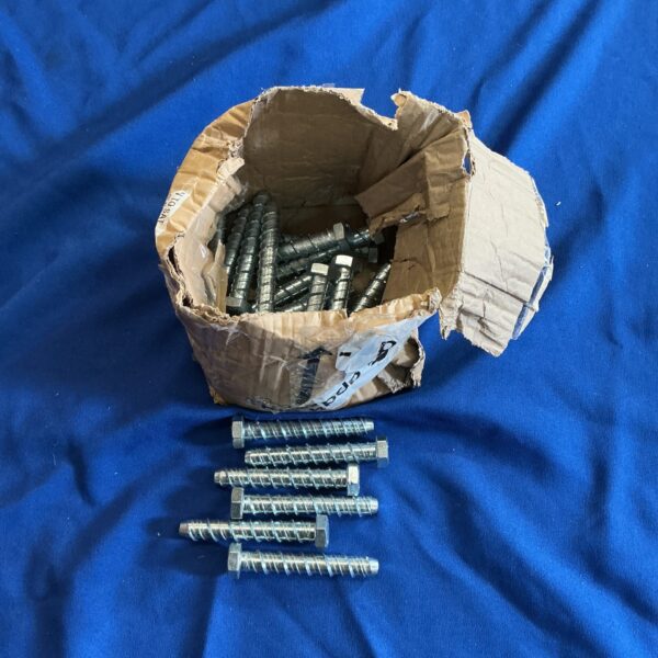 Steel hex anchor bolts inside a damaged cardboard box.