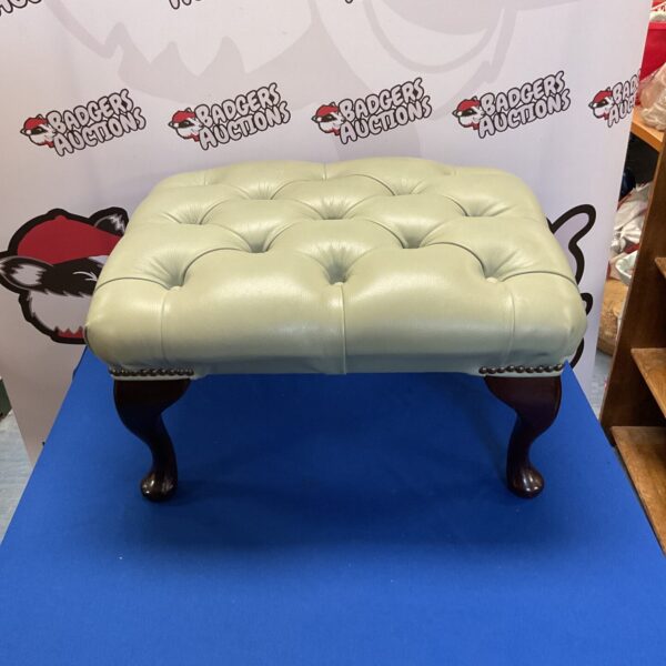 Vintage leather footstool with wooden legs, classic home decor.