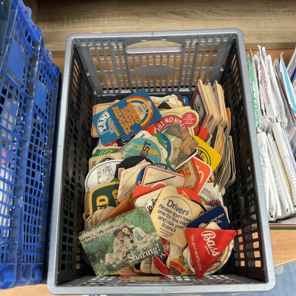 Crate of mixed vintage and modern pub coasters.
