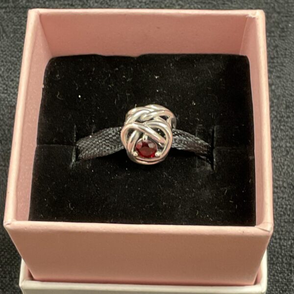 Close-up of a Pandora red stone charm on a pink background.