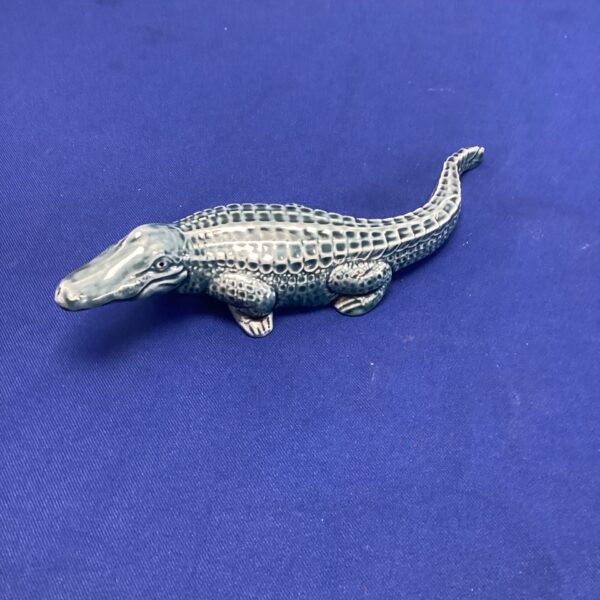 Vintage Poole Pottery crocodile figurine on blue background.