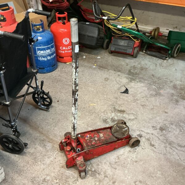 Red trolley jack in a garage setting, showing signs of wear.