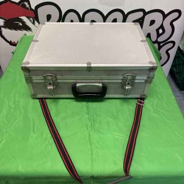 Silver aluminium travel case with red strap, open on green surface.