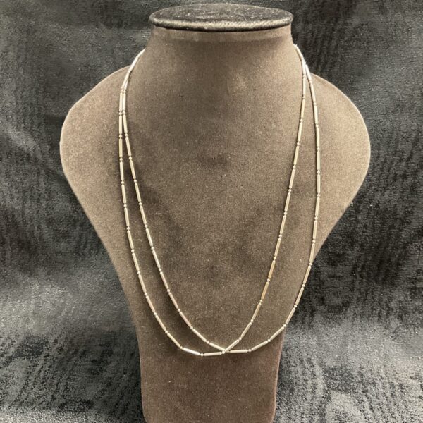 Two delicate silver bar link necklaces on a display bust.