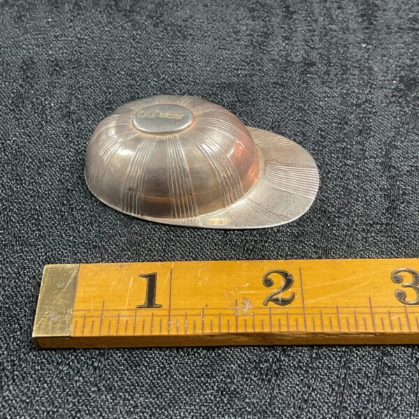 Silver jockey cap caddy spoon displayed with a measuring ruler.