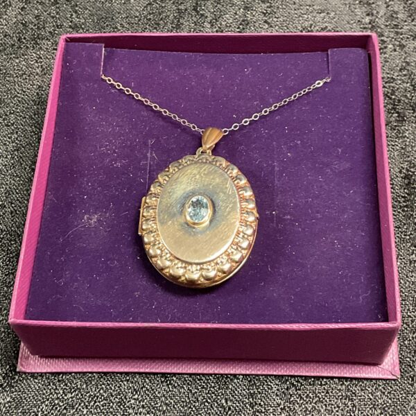 Antique silver locket with vibrant topaz gemstone on a chain.
