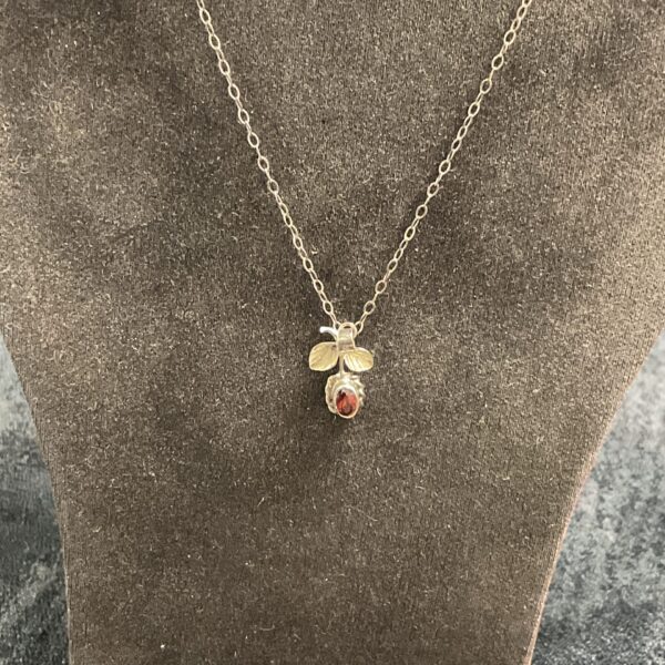 Close-up of sterling silver strawberry pendant with garnet gemstone.
