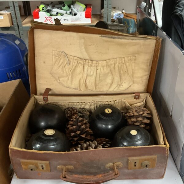 Vintage bowling balls in a worn leather case with pine cones.