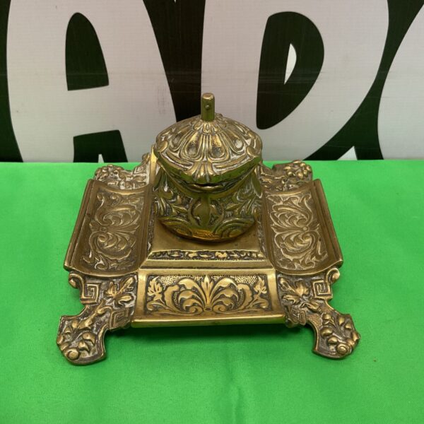 Ornate vintage brass inkwell on a dark surface.