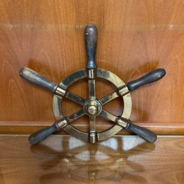 Polished brass ships wheel with missing handle, nautical decor.