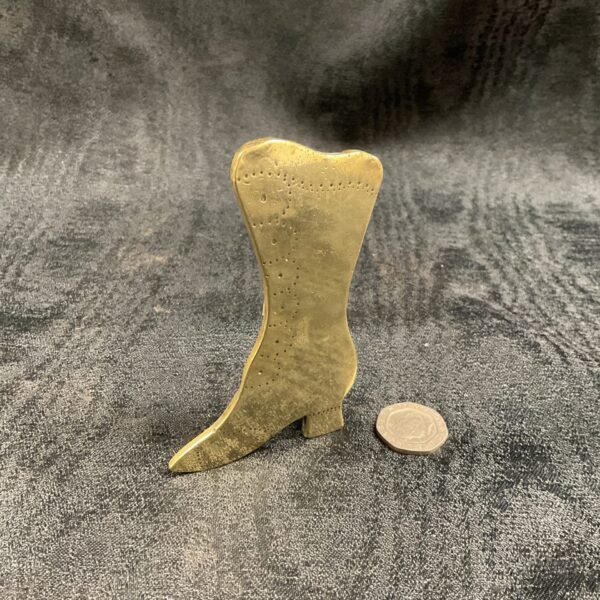 Vintage brass trench art boot on dark background.