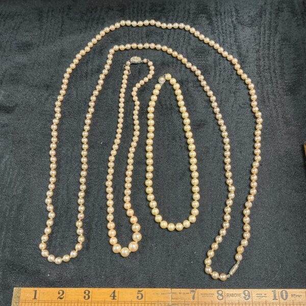 Vintage lot of three faux pearl necklaces on a neutral background.