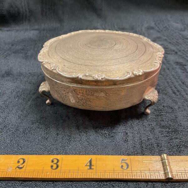 Front view of a vintage silver trinket box with embossed details.