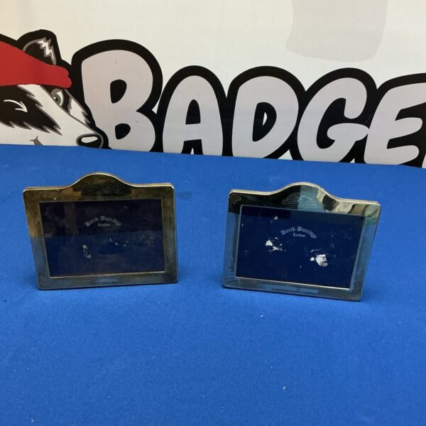Two vintage silverplate photo frames on a dark surface.