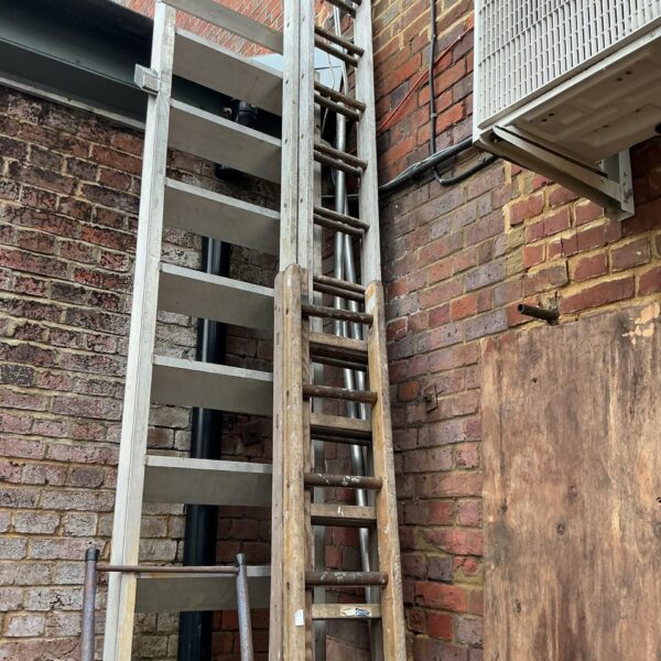 Vintage wooden extending ladder leaning against brick wall.