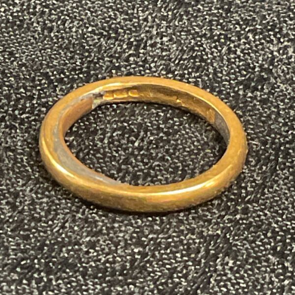 Close-up of a hallmarked 22ct gold band ring on a textured surface.
