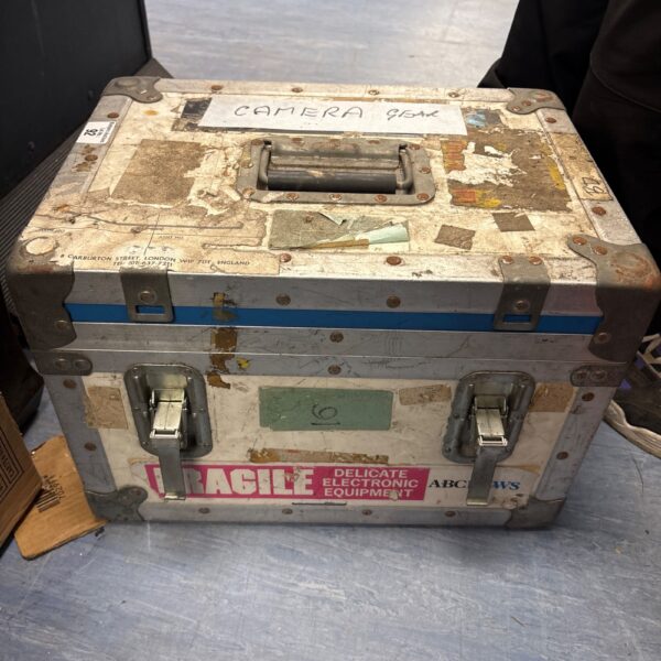 Well-used aluminium flight case with "CAMERA GEAR" label.