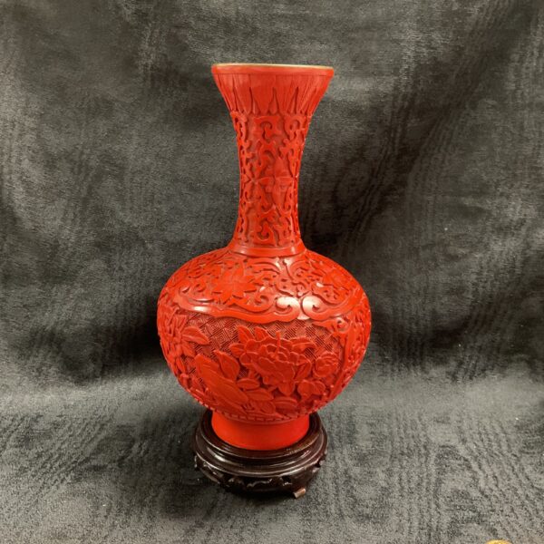 Intricate red cinnabar vase with floral carvings on a brass base.