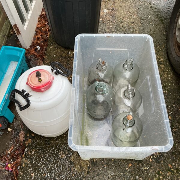 Lot of five glass demijohns and a plastic barrel for storage.
