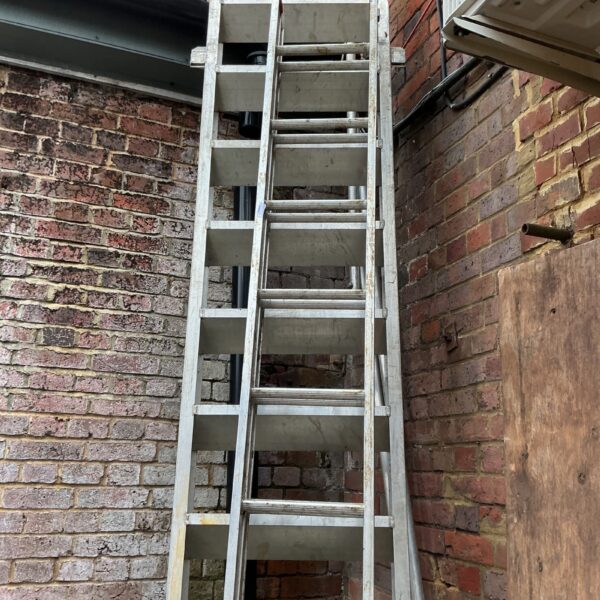 Silver double aluminium extension ladder leaning against a brick wall.