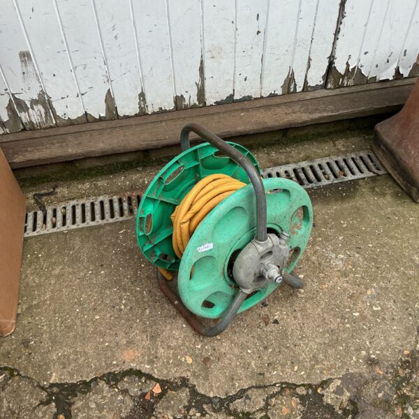 Vintage green garden hose reel with hose wound around it.
