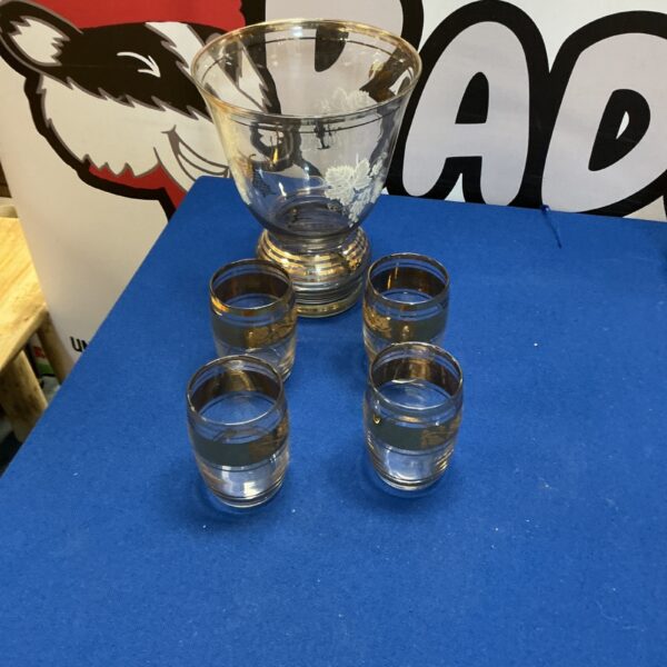 Vintage glass vase and tumblers with gold rims on a blue surface.