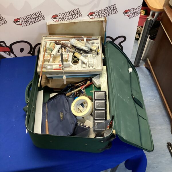 Vintage green suitcase filled with art supplies and painting materials.