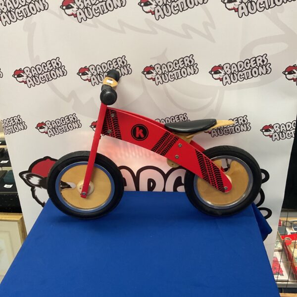 Red Kiddimoto Kurve wooden balance bike for young children.