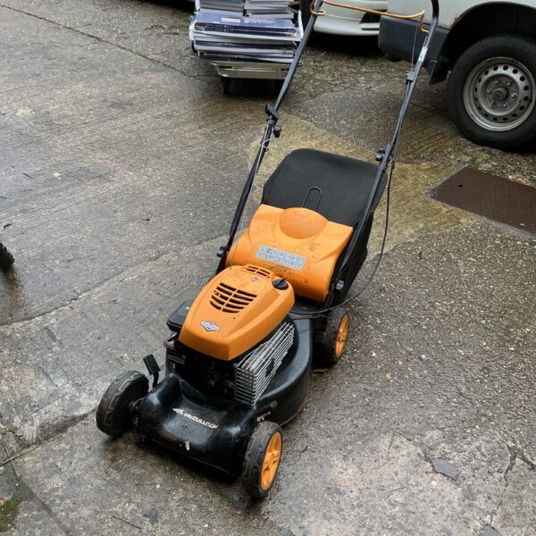 Side view of a used McCullough petrol lawnmower in a garden.