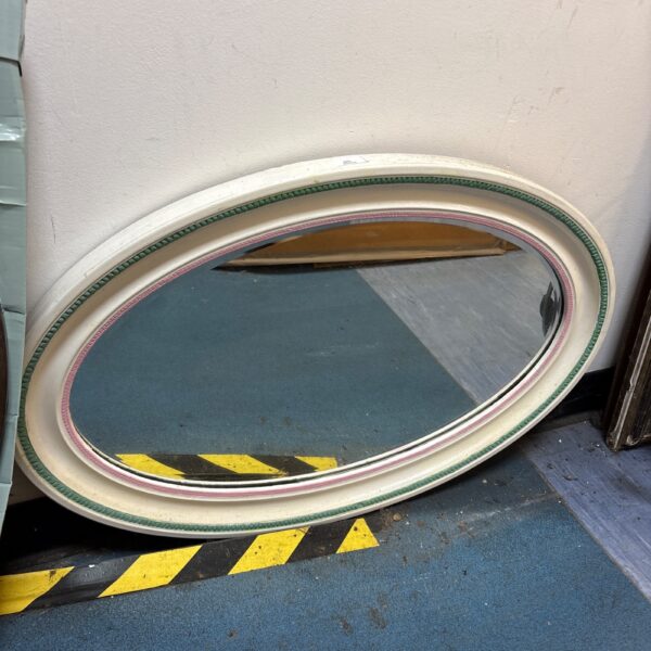 Vintage oval wall mirror with gilded frame and subtle colour accents.