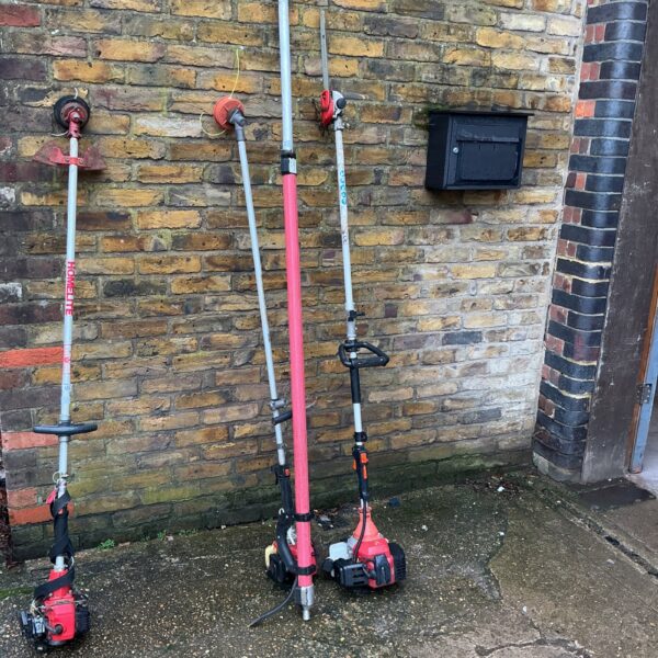 Two petrol strimmers with pole attachment in a garden setting.