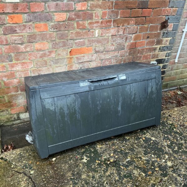 Weathered plastic garden storage box for outdoor use.