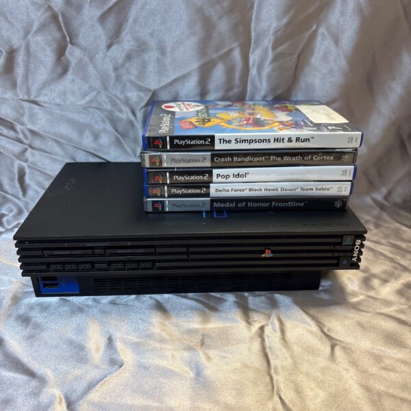 Black PlayStation 2 console with game cases stacked beside it.