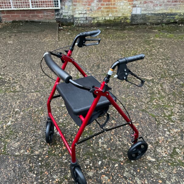 Red mobility walker with padded seat and four wheels.