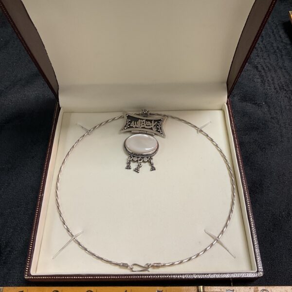 Intricate silver torque necklace with Arabic calligraphy and white stone.