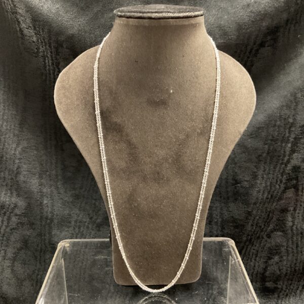 Delicate silver ball link necklace on a display stand.